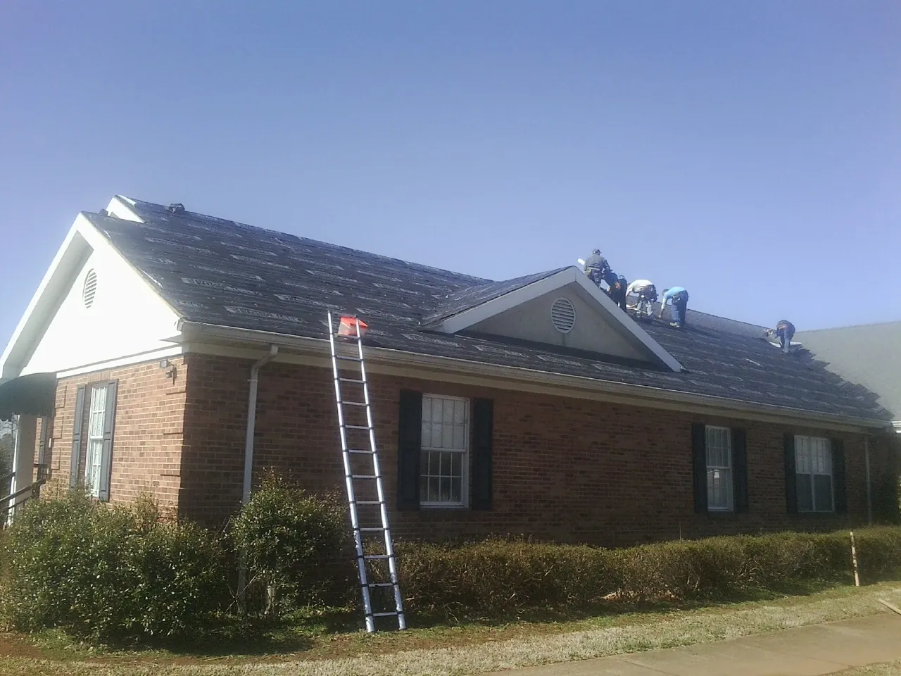 Crew tearing shingles off a brick ranch roof with a ladder set — Emergency Roof Repair work by our crew in Pe Ell