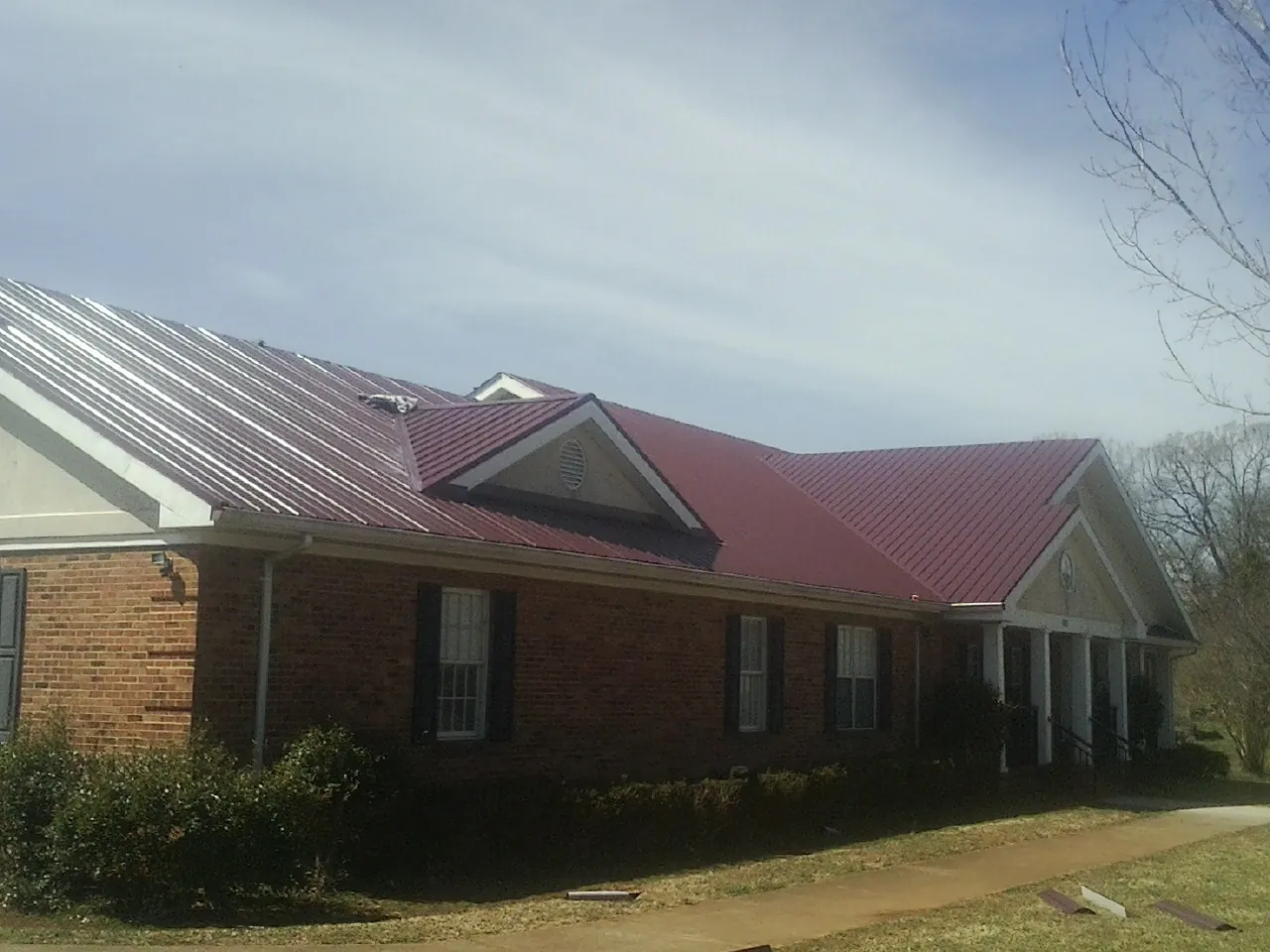 Red metal roof with gabled entries on a long brick building, from a Hail Damage Roof Repair job in Pe Ell