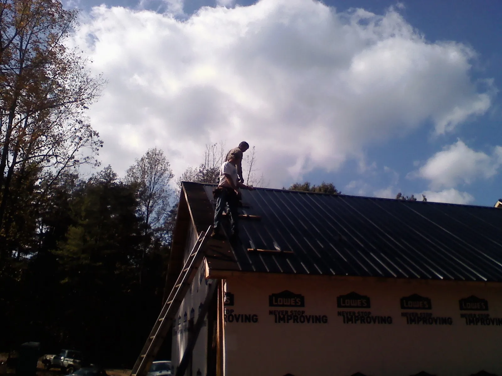 Roofer fastening dark metal panels high against a cloudy sky in Pe Ell