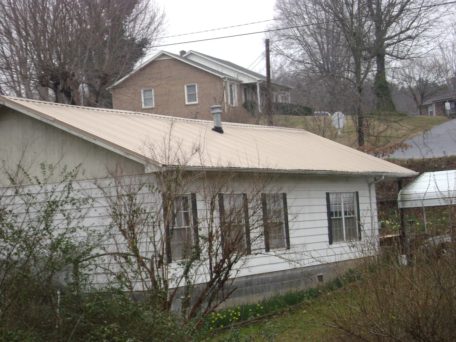 Tan metal roof on a white sided house set into a hillside — Commercial Roofing by Roofing Brothers in Pe Ell